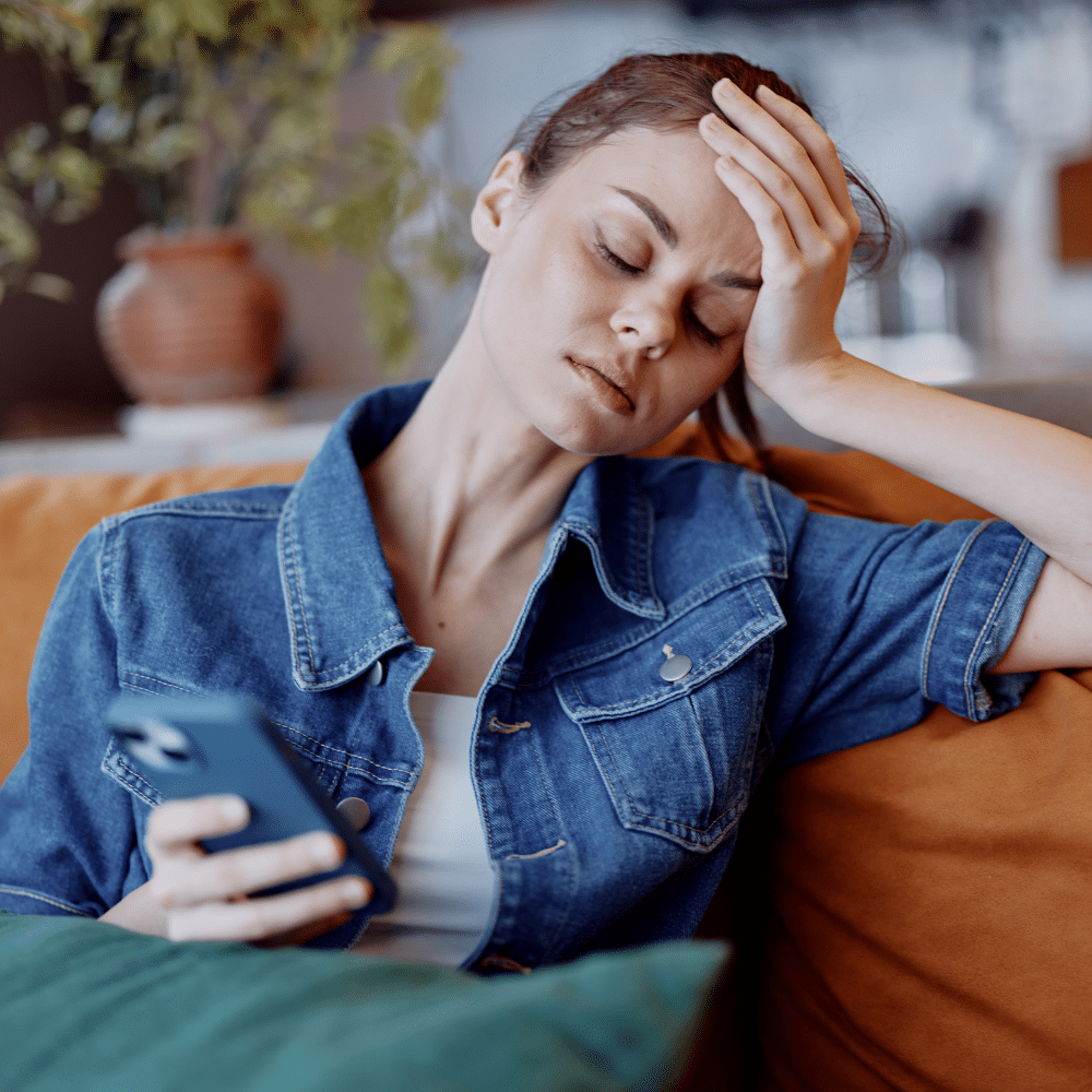 Woman sitting on couch looking exhausted while scrolling her phone — illustration of doomscrolling habit